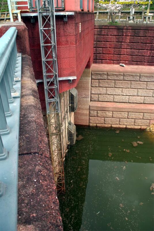 曇天の下、ダムの上から脇に設置された排水部を見る。水位が下がっている。｜新滝の池｜大阪府泉佐野市上之郷｜2026年04月05日