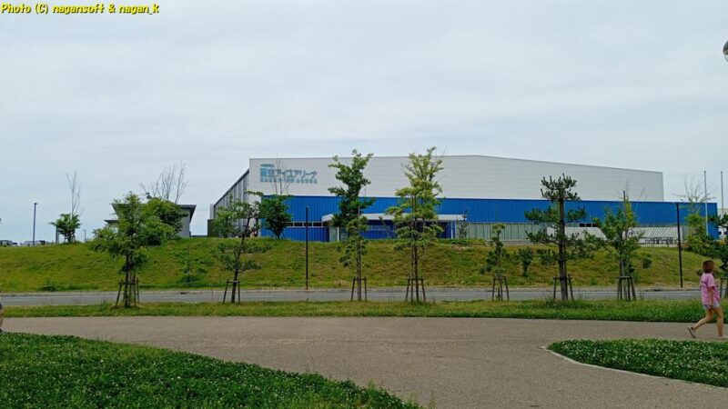 「いずみさのカレーサミット2026」イベント会場から「関空アイスアリーナ」を見る。曇天の下、ジョギング中の女性が前を横切る｜大阪府泉佐野市｜2026年05月31日撮影