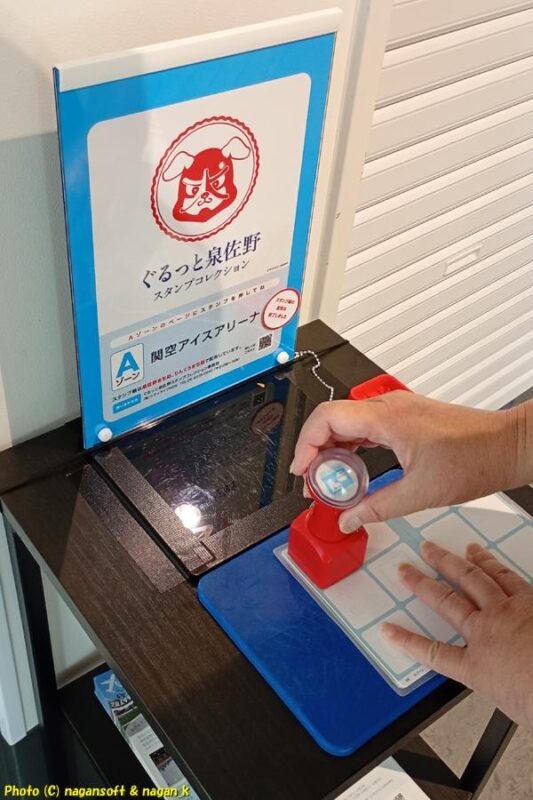 「関空アイスアリーナ」ロビーに設置されている「ぐるっと泉佐野スタンプコレクション」押印台とスタンプ。スタンプ帳を広げてスタンプを押印している｜大阪府泉佐野市｜2026年05月31日撮影
