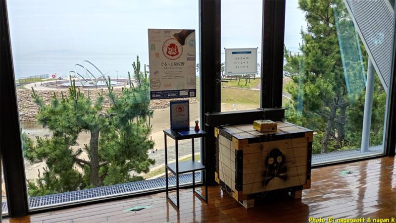 りんくう公園内の「総合休憩所」２階の休憩スペース。大きな宝箱と「ぐるっと泉佐野スタンプコレクション」押印台とスタンプが設置されている。その向こうはガラス張りで海岸が見えている｜大阪府泉佐野市｜2026年05月31日撮影