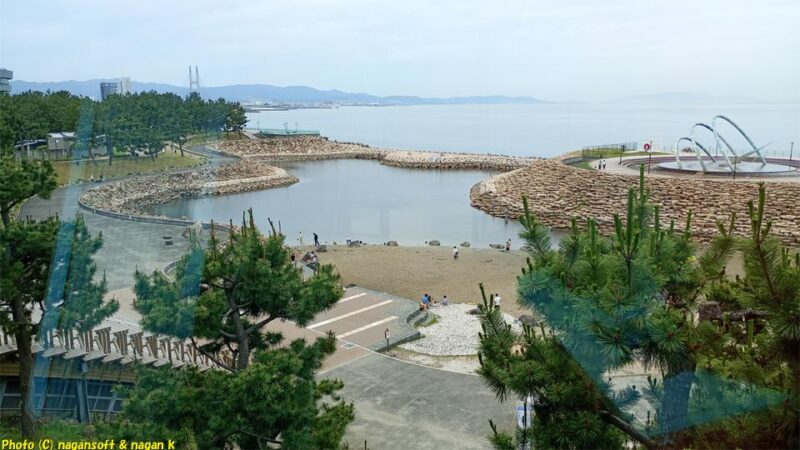 りんくう公園内「総合休憩所」２階の休憩スペースから和歌山方面を見る。りんくう公園“内海”の向うに海岸線が伸び、大きな吊橋と和歌山までの海岸線が見える。曇り空で風はなく海は凪いでいる｜泉佐野市｜2026年05月31日撮影